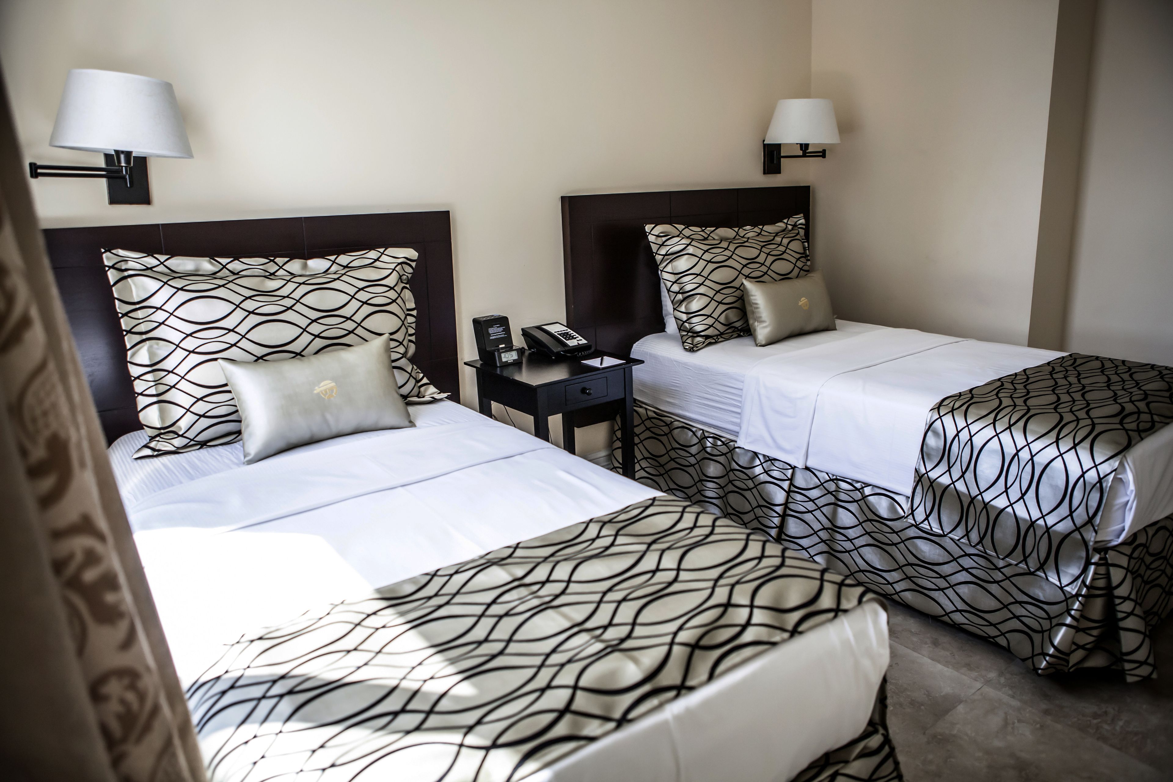 Camera d'albergo con due letti, ciascuno con una coperta a motivi decorativi, un comodino con una lampada e un telefono.