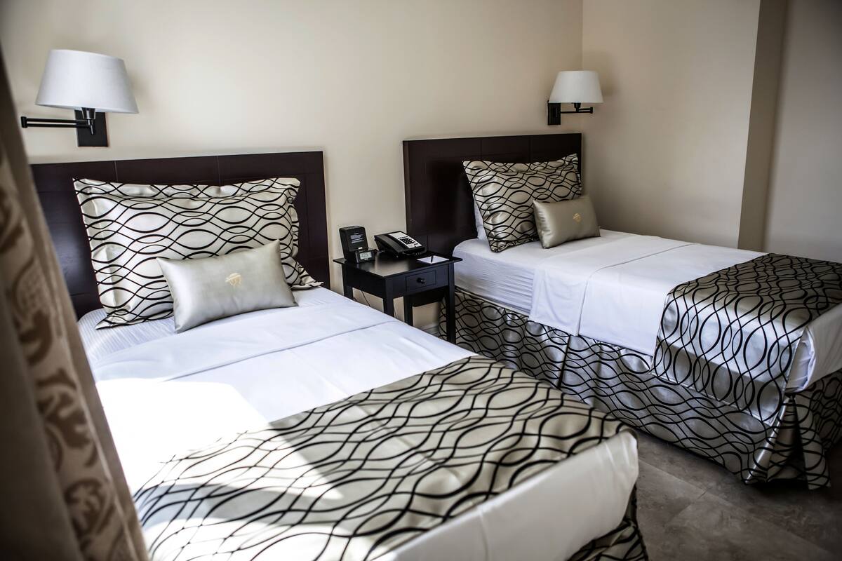 A hotel room with two beds, each with a patterned bedspread, a bedside table with a lamp, and a phone.