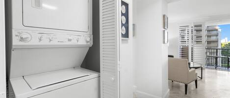 A laundry room with stacked washers and dryers, a chair, and a view of a balcony with outdoor furniture.