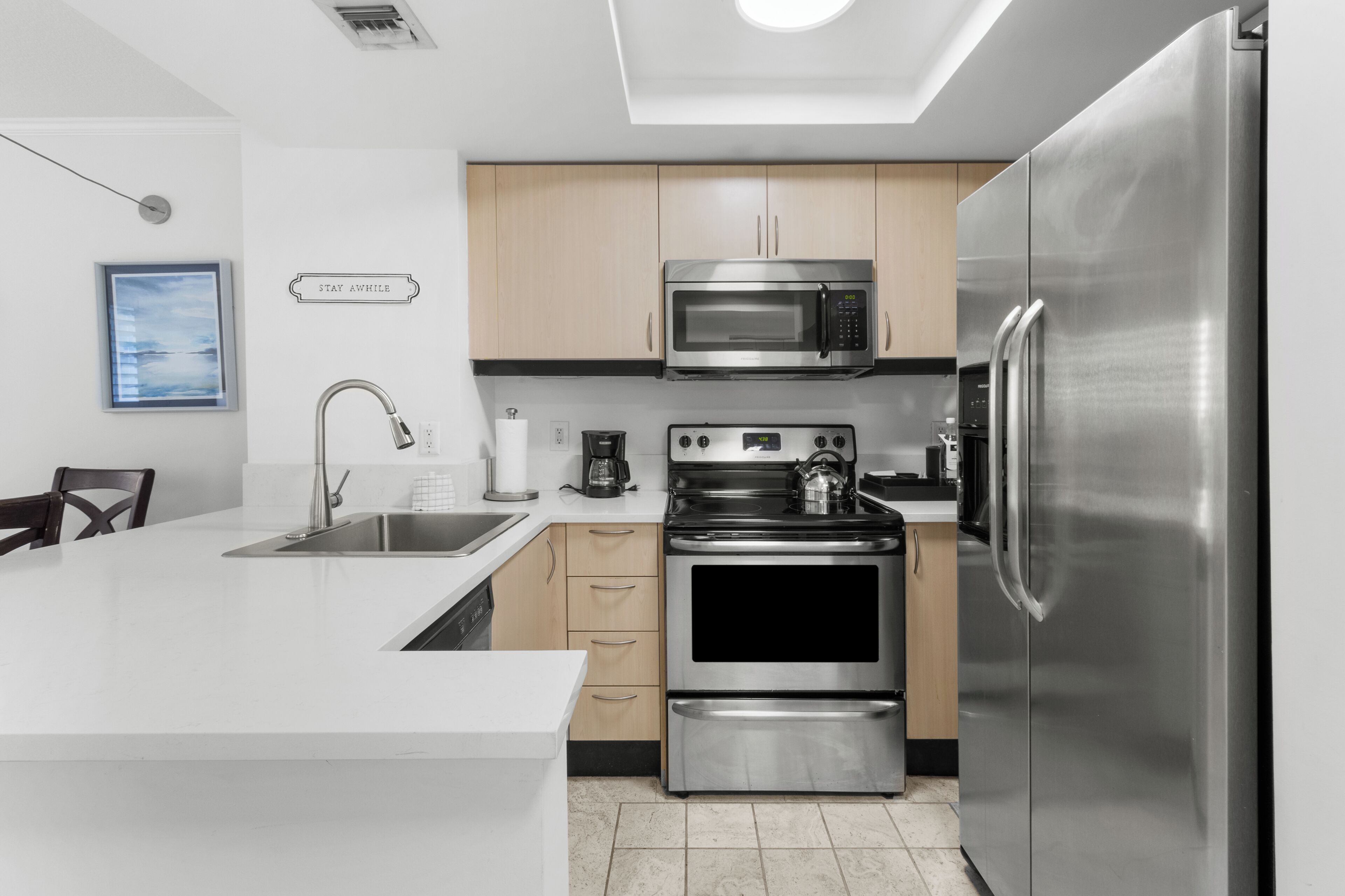 A modern kitchen with stainless steel appliances, a white countertop, and wooden cabinets.