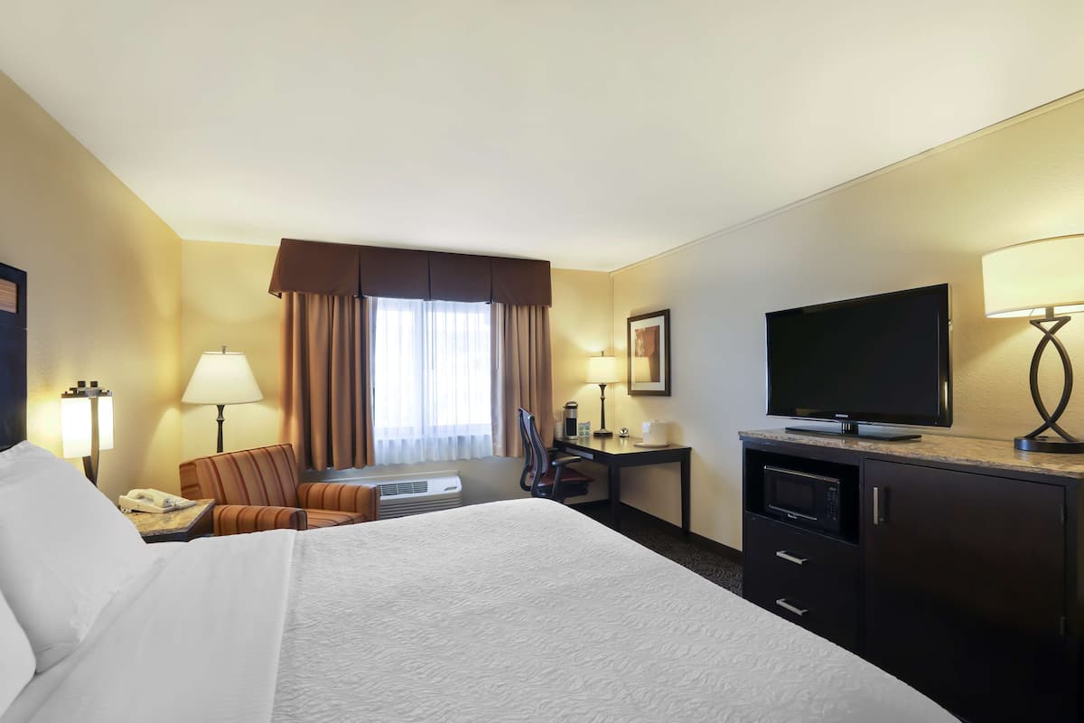 A hotel room with a large bed, a desk with a flat-screen TV, a microwave, and a telephone.
