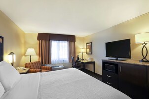 A hotel room with a large bed, a desk with a flat-screen TV, a microwave, and a telephone.