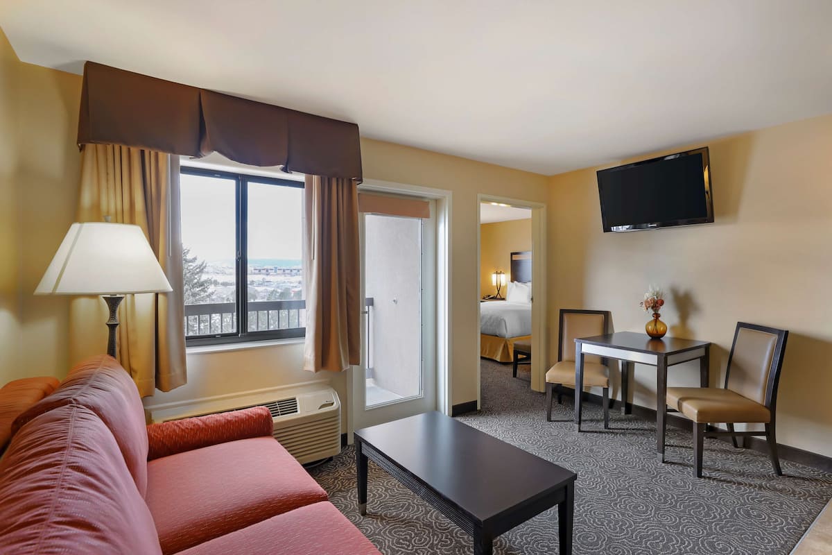 A hotel room with a sofa, a table, a TV, and a view of the outdoors.