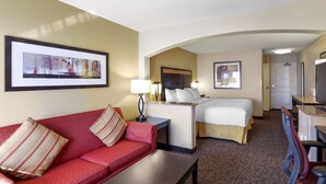 Une chambre d’hôtel avec un canapé rouge, un lit avec une literie blanche, un bureau avec une lampe et un téléviseur.