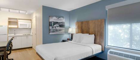 Une chambre d’hôtel équipée d’un lit, d’un bureau, d’un four à micro-ondes et d’une fenêtre avec des stores.