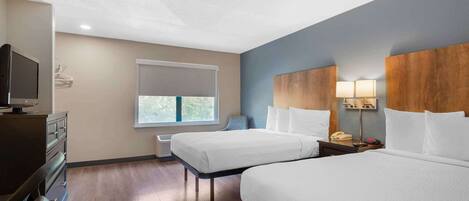 A hotel room with two beds, a TV, a desk, and a window with a view.