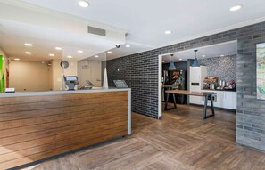 A reception area with a wooden reception desk, a black brick wall, and a dining area with a table and chairs. - Extended Stay America Suites San Francisco San Mateo SFO (San Mateo)
