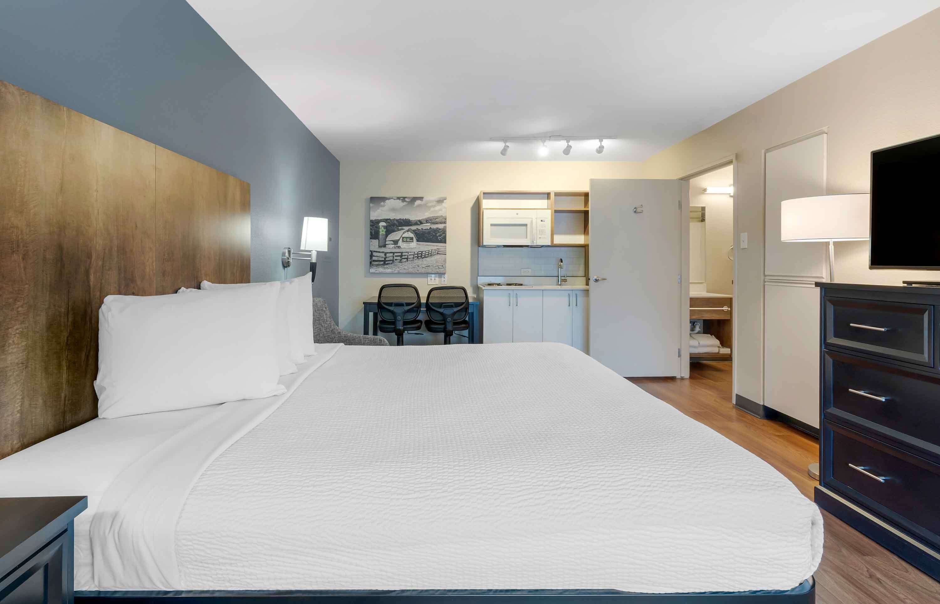 Camera d'albergo con un letto grande, una scrivania con due sedie, un angolo cottura, una TV e un armadio.