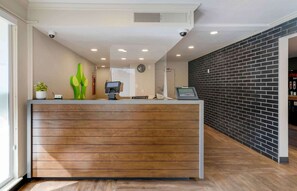 A reception desk with a wooden panel design, a potted plant, and a security camera above. - Extended Stay America Suites San Francisco San Mateo SFO (San Mateo)