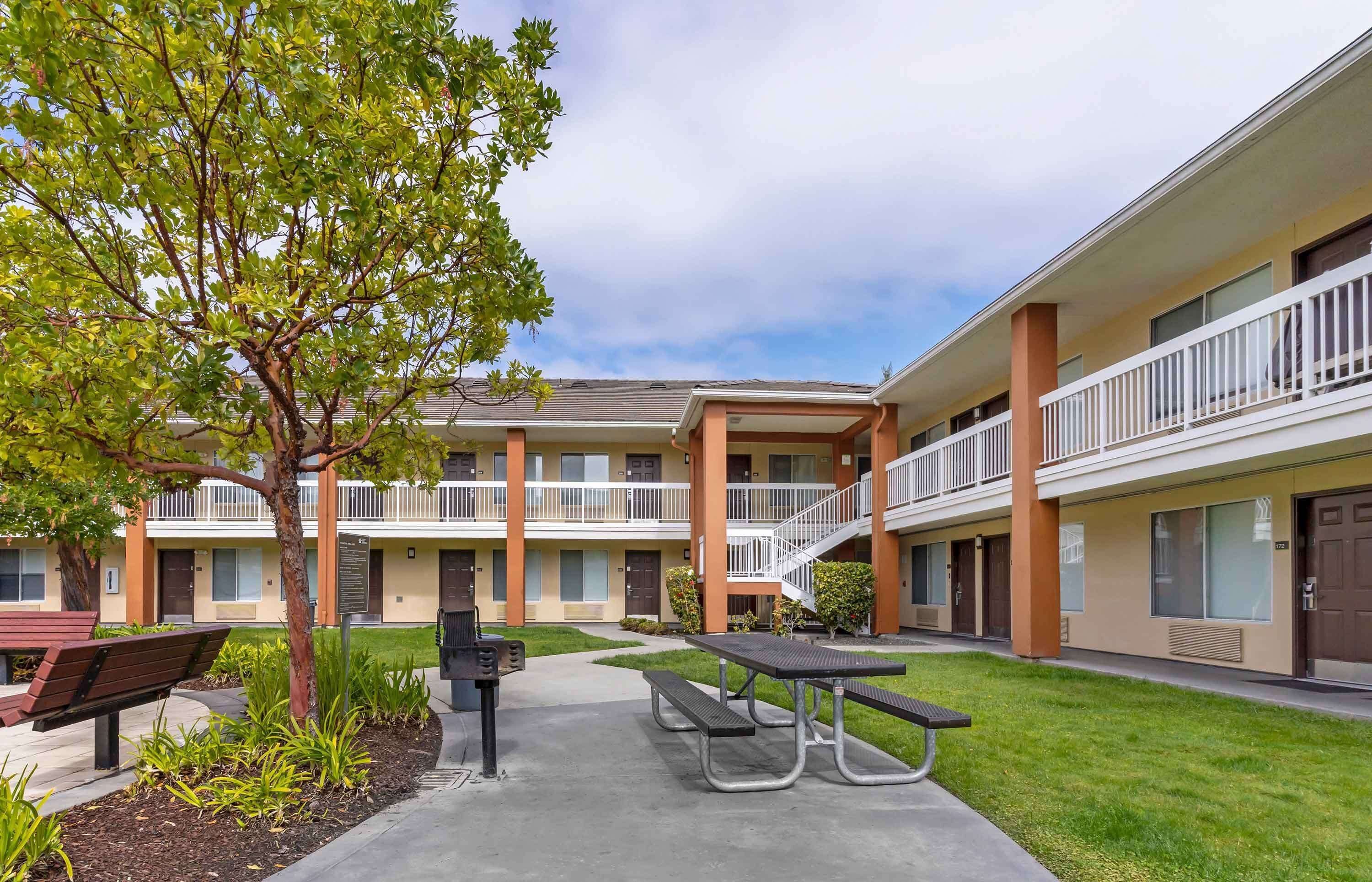 A multi-story motel with outdoor seating, a covered patio, and a staircase connecting the floors.