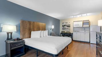 A hotel room with a bed, bedside table, lamp, phone, and a kitchenette with a microwave, refrigerator, and cabinets.