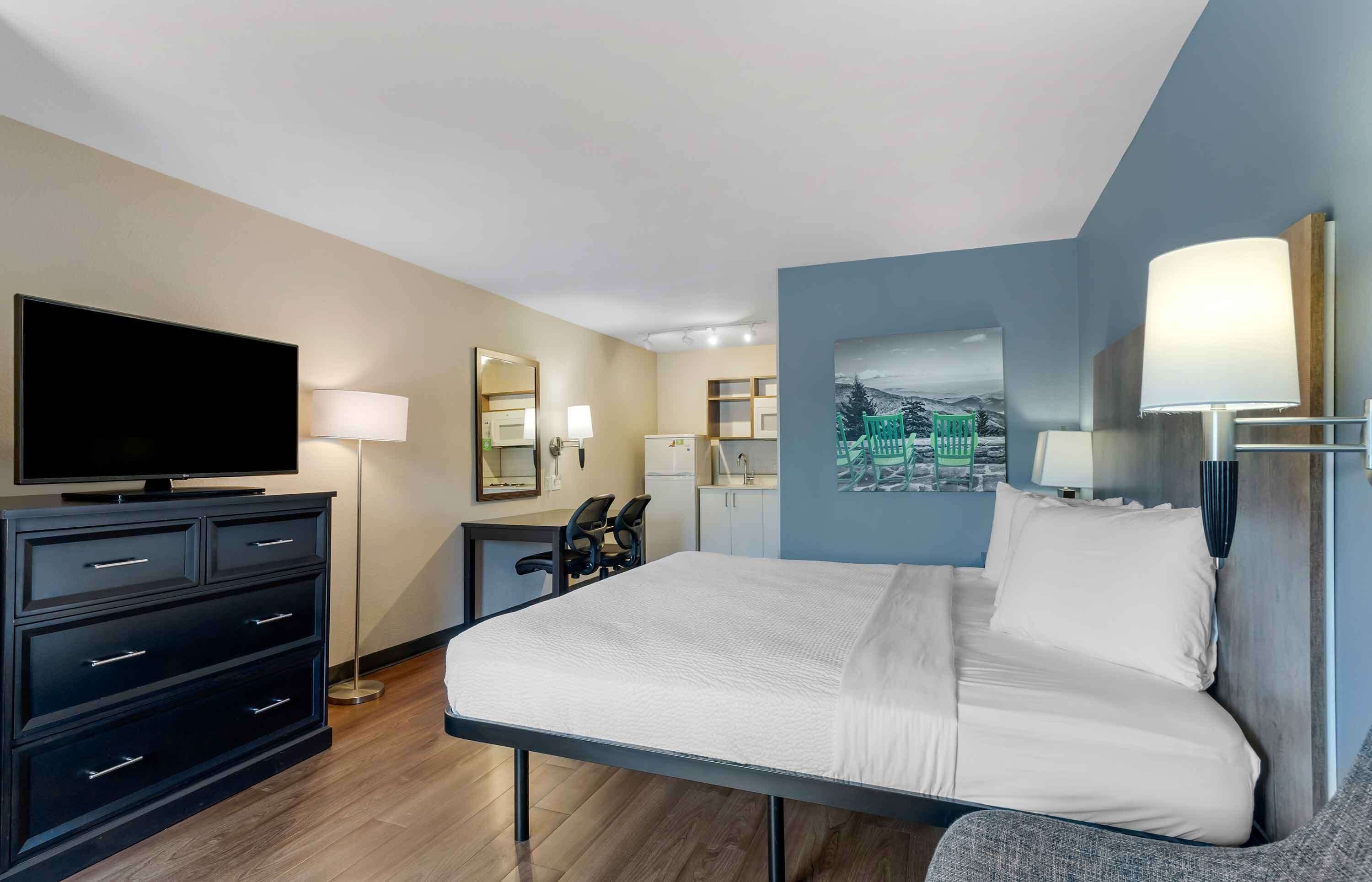 A hotel room with a bed, a flat-screen TV, a dresser, a desk, and a chair.