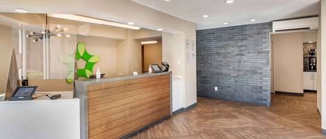 A reception area with a wooden reception desk, a green abstract wall art, and a brick wall.