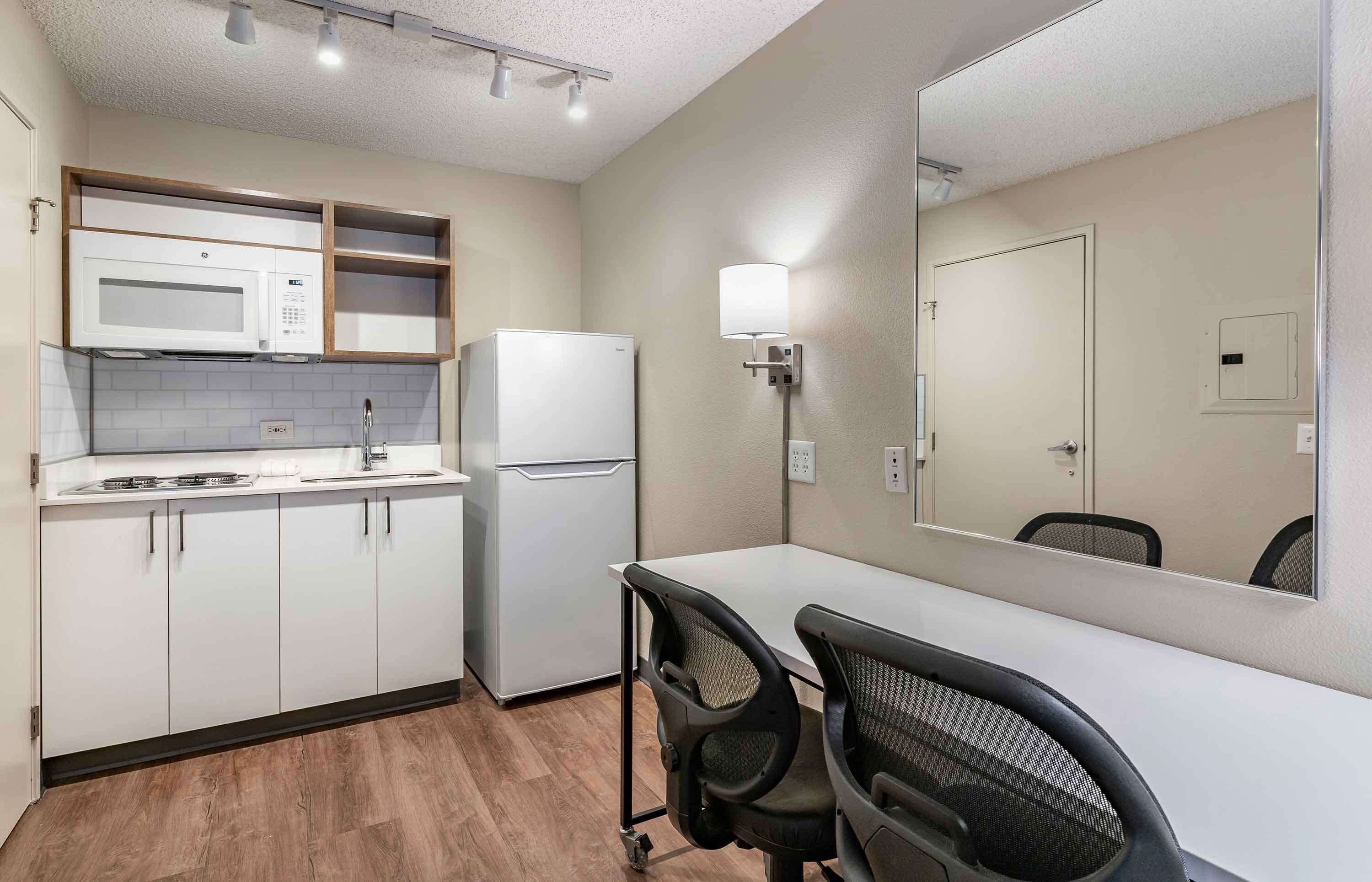 A compact kitchenette with a microwave, stove, and refrigerator, a small dining table with chairs, and a wall-mounted light fixture.