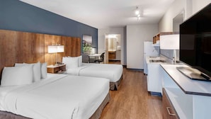 Habitación de hotel con dos camas, un escritorio, un televisor y un baño visible al fondo.