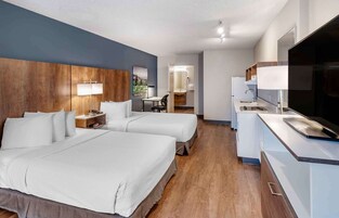 Habitación de hotel con dos camas, un escritorio, un televisor y un baño visible al fondo.