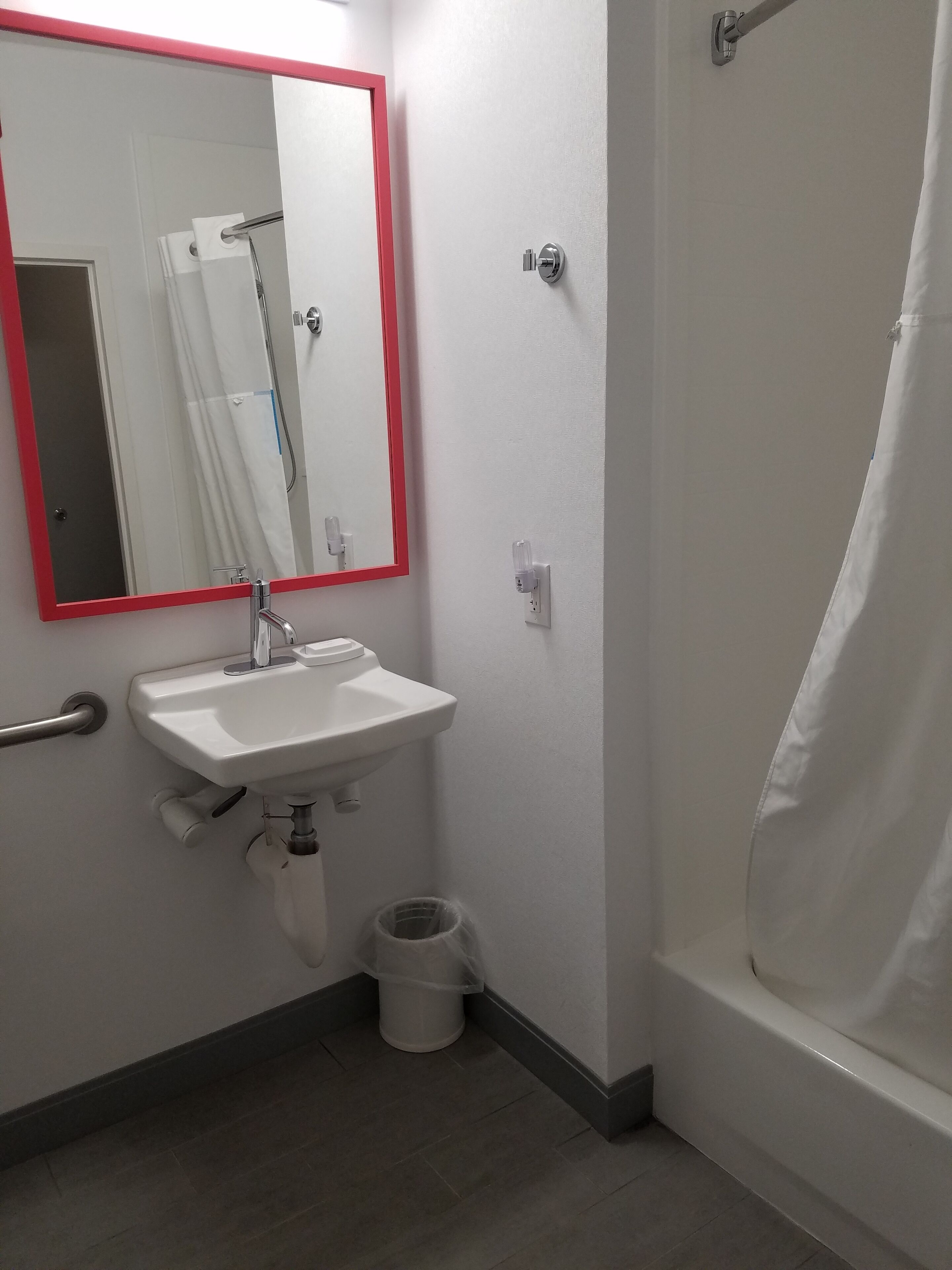 Une salle de bain avec un lavabo blanc, un miroir avec un cadre rouge, un rideau de douche et des toilettes.