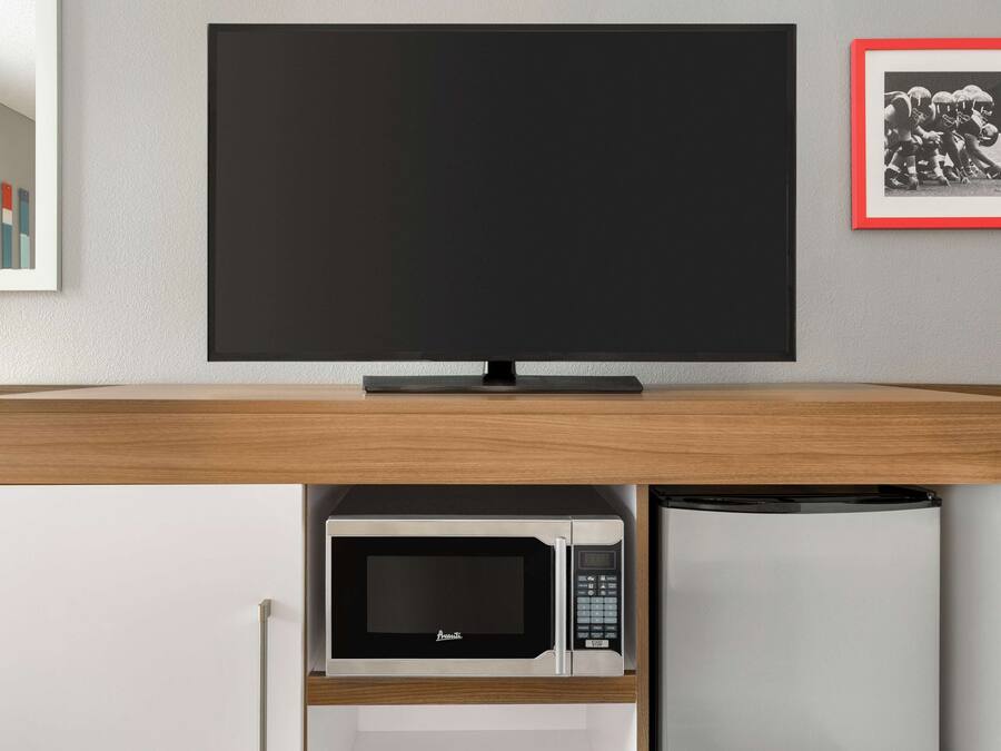 A modern kitchen with a built-in microwave and refrigerator, a flat-screen TV, and a framed picture on the wall.