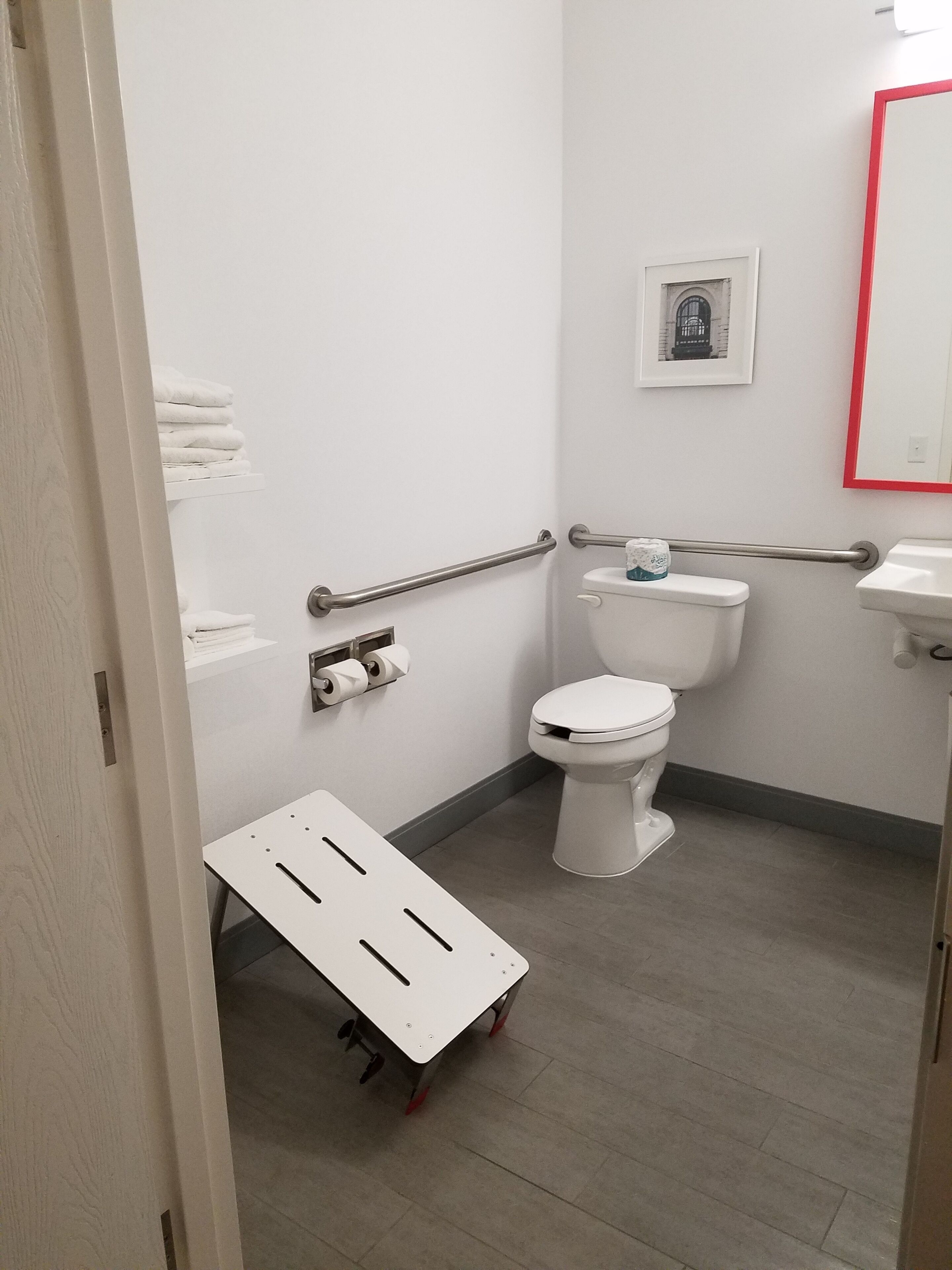 Un baño con inodoro, lavamanos, baranda y un pequeño estante con toallas.