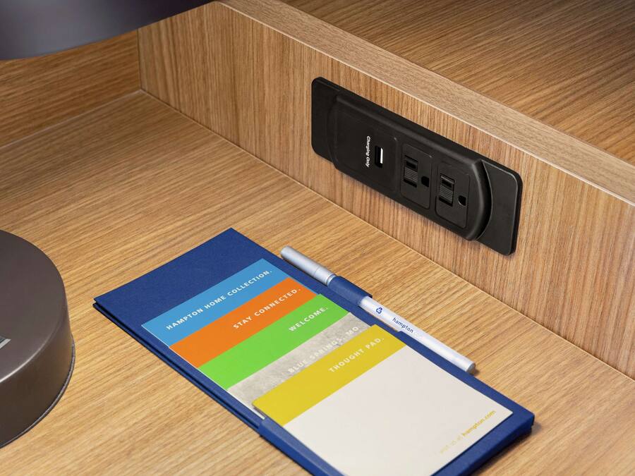 A notebook with a pen, a power outlet, and a charging station on a wooden surface.