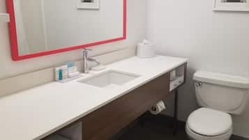 A modern bathroom with a white sink, a mirror with a red frame, a toilet, and a small framed picture on the wall.