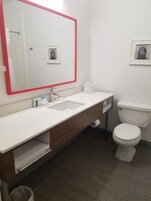 A modern bathroom with a white sink, a mirror with a red frame, a toilet, and a small framed picture on the wall.