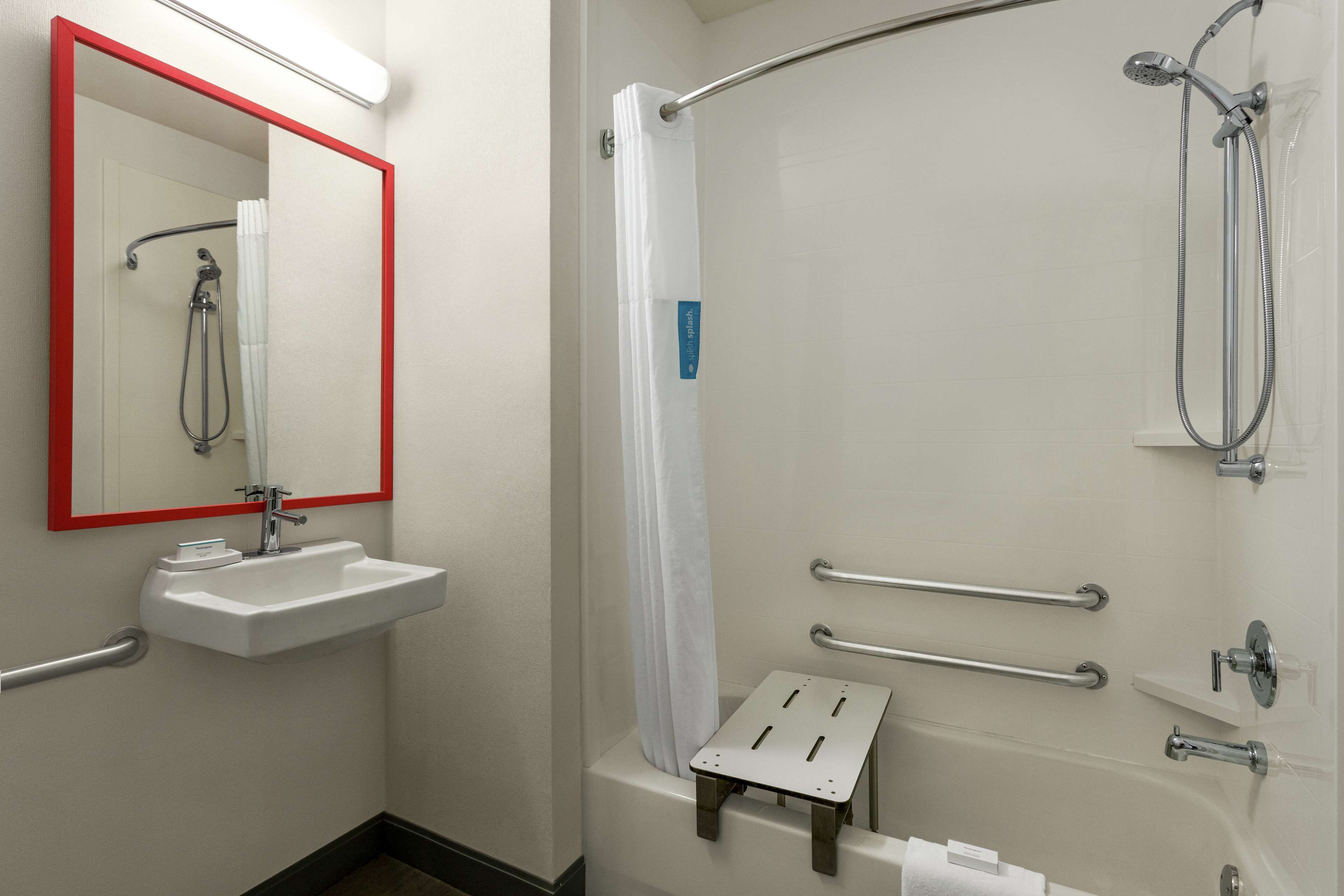 Un baño con lavamanos, espejo, ducha y barras de apoyo.