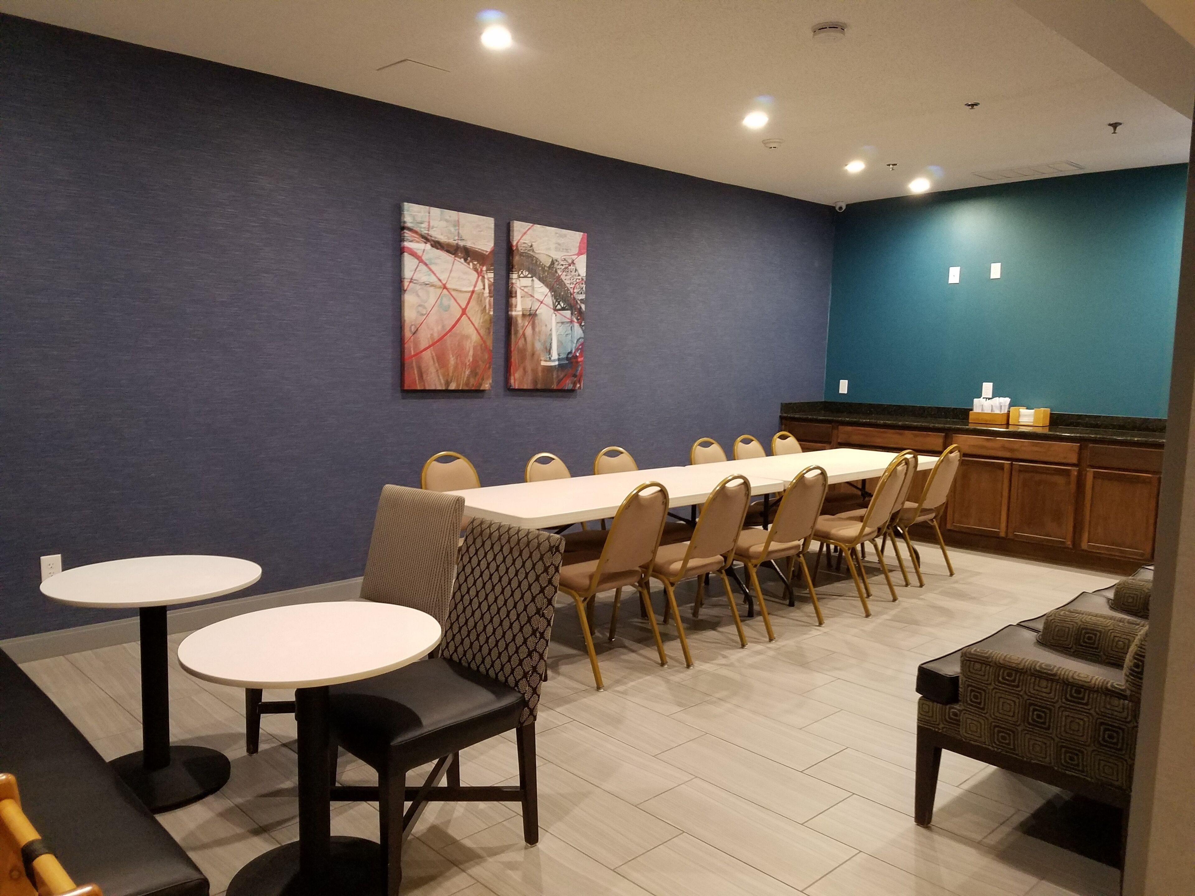 A dining area with a long table and chairs, a smaller round table, and a kitchen area with a counter and cabinets.