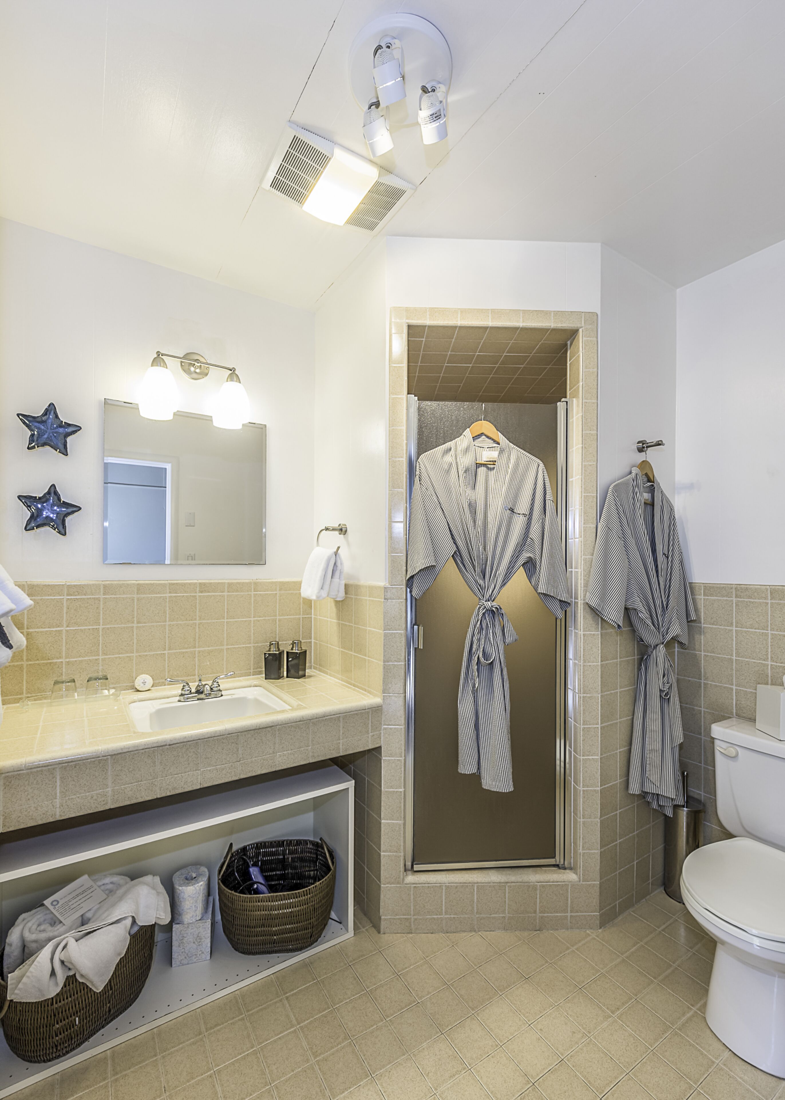 Une salle de bain équipée d'un lavabo, d'un miroir, de patères pour peignoirs et d'une douche.