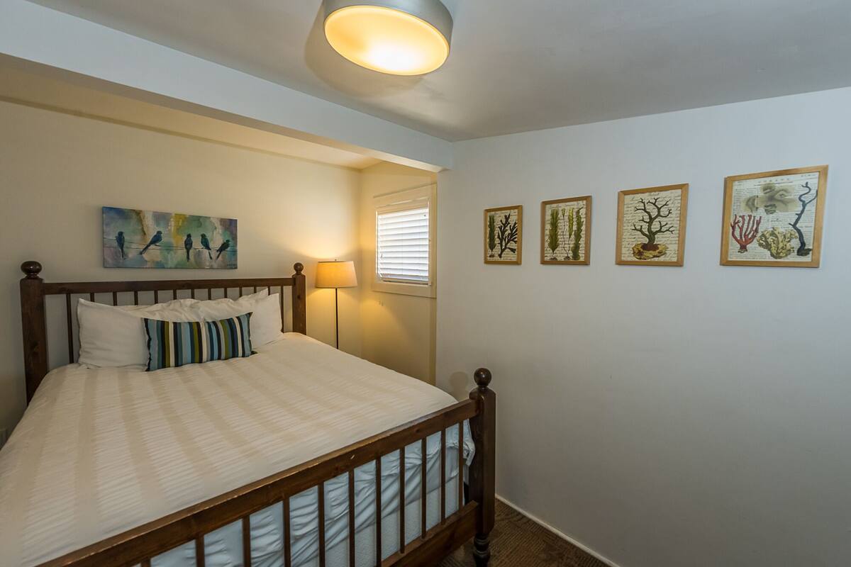 A bedroom with a wooden bed, a nightstand, a lamp, and wall art.