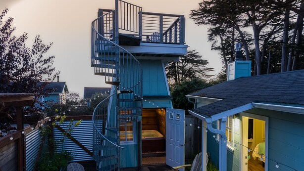 Una casa azul de dos pisos con una escalera espiral que lleva a un balcón.