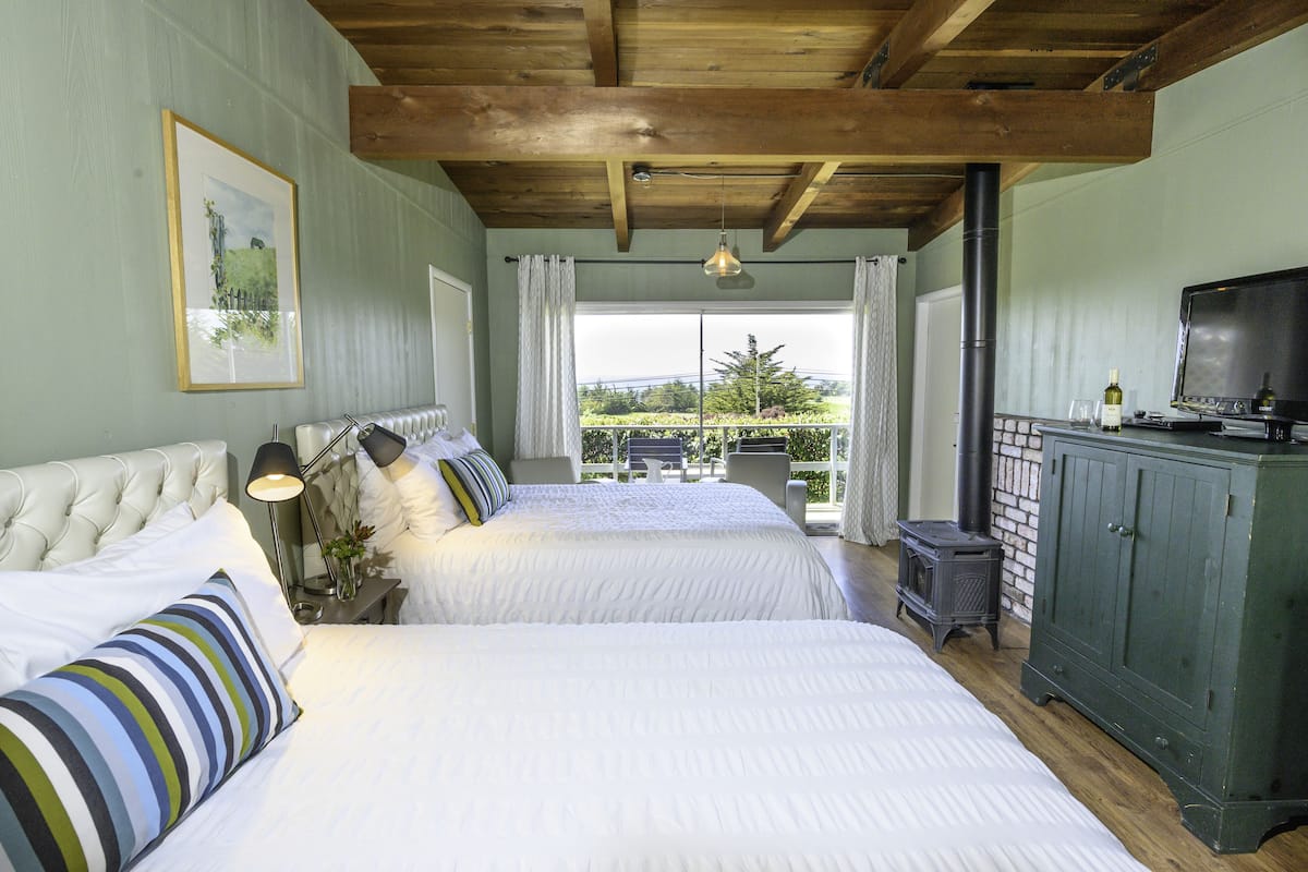 A bedroom with two beds, a wooden ceiling, a television, and a view of the outdoors.