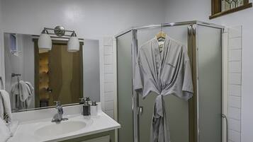 Une salle de bain avec un lavabo blanc, un miroir, une robe suspendue à la porte de la douche et des toilettes.