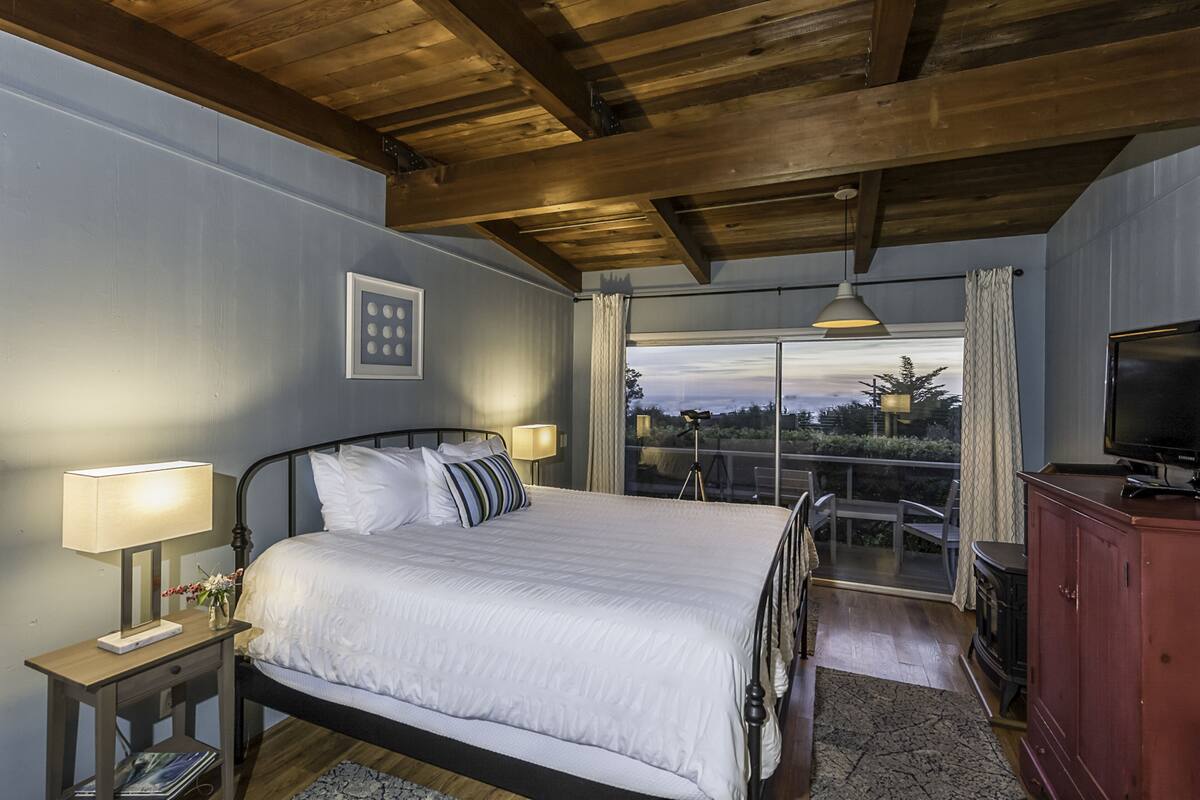 A bedroom with a bed, bedside lamps, a TV, a wooden cabinet, and a balcony with a view.