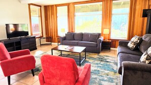 Una sala de estar con un sofá, dos sillones, una mesa de centro, un televisor y una lámpara.