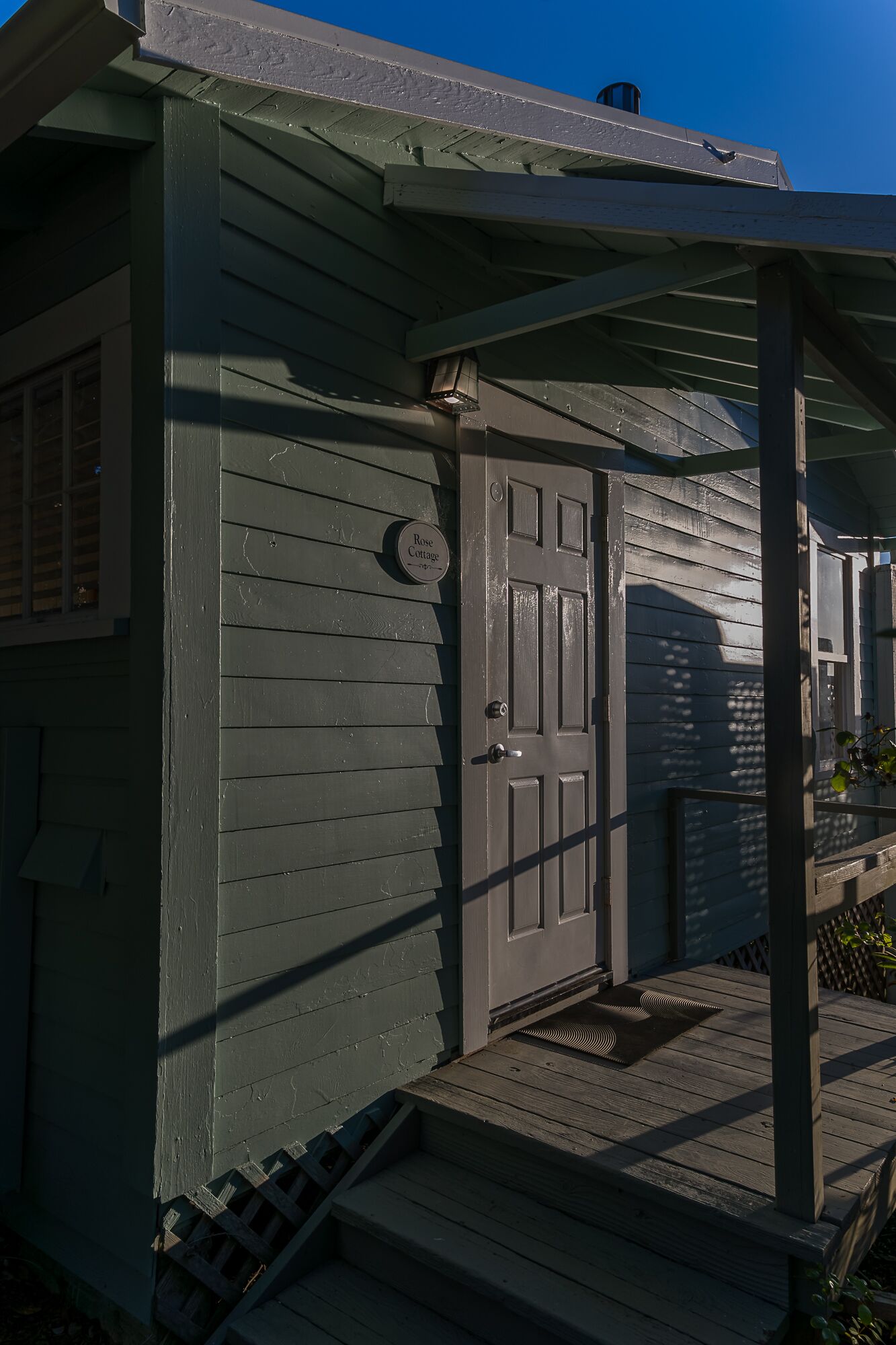 A small, single-story building with a dark green exterior, a front door, and a porch.