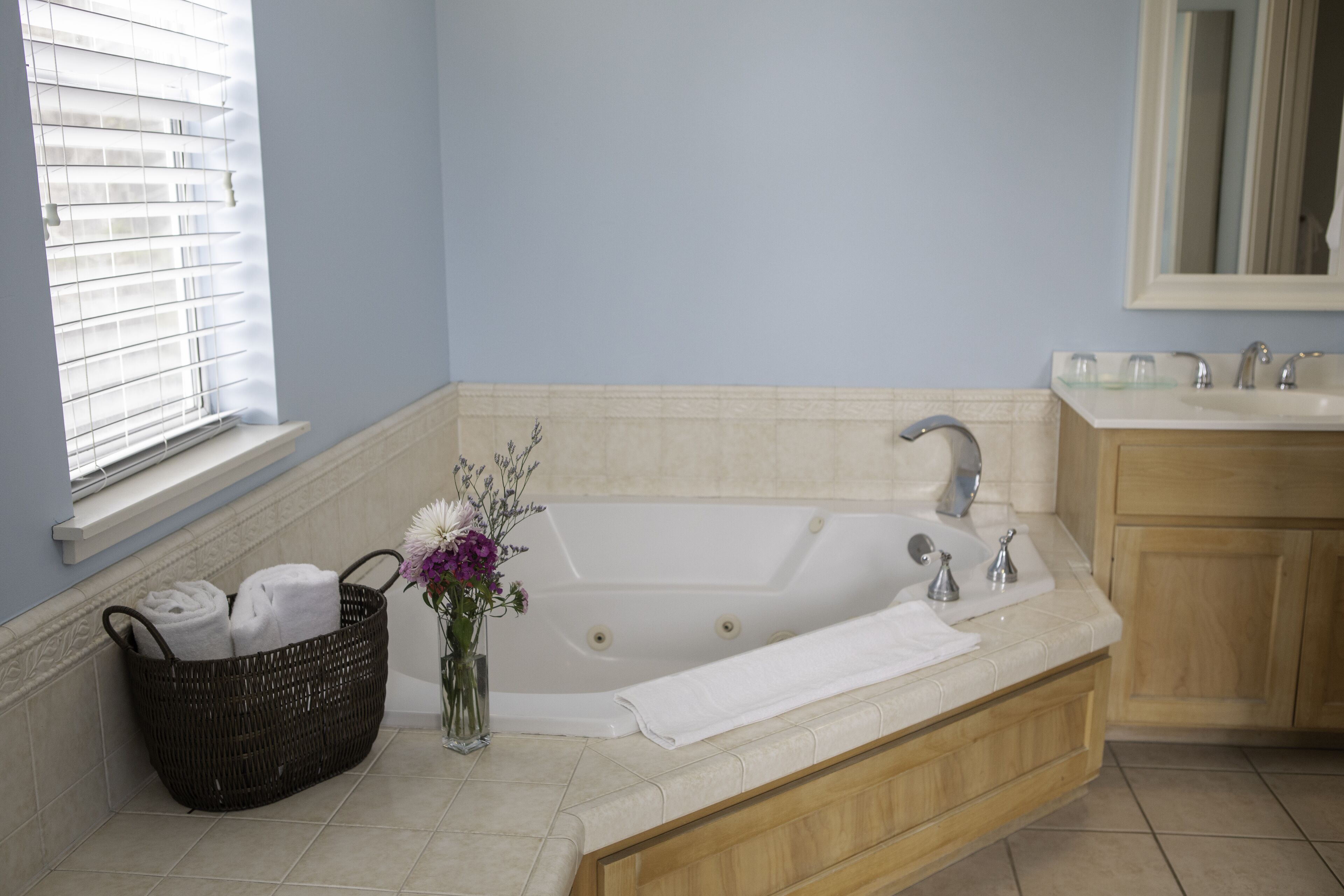 A bathroom with a bathtub, a sink, a mirror, and a window with blinds.