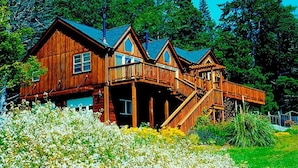 A large wooden cabin with multiple balconies, surrounded by a lush garden. - The Inn at Schoolhouse Creek (Little River)