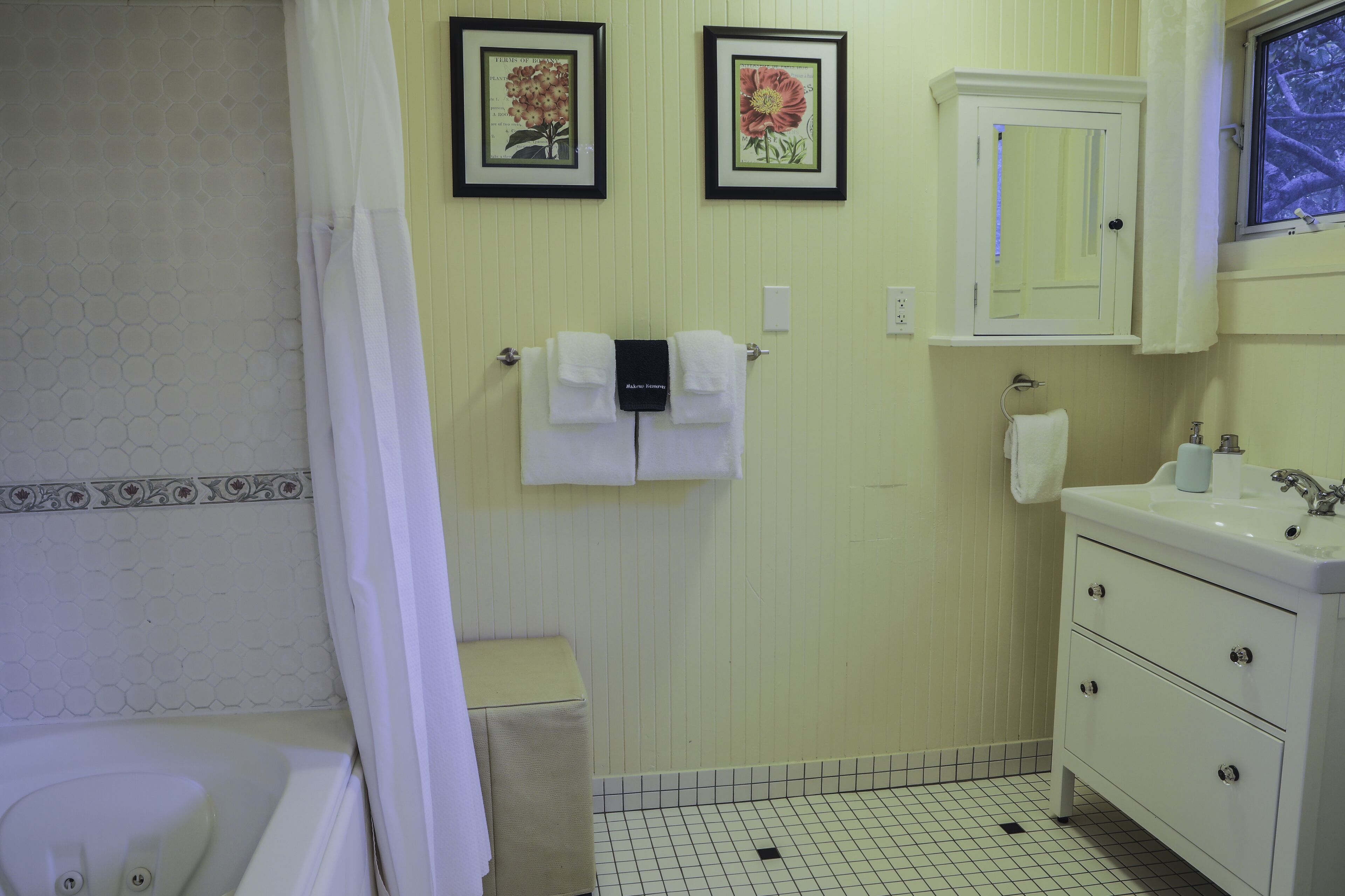 A bathroom with a white bathtub, a sink, and a mirror above the vanity. There are two framed floral pictures on the wall.