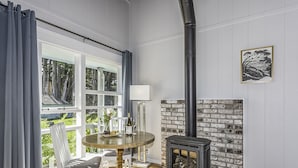 A room with a fireplace, a dining table with chairs, a window with curtains, and a view of greenery outside. - The Inn at Schoolhouse Creek (Little River)