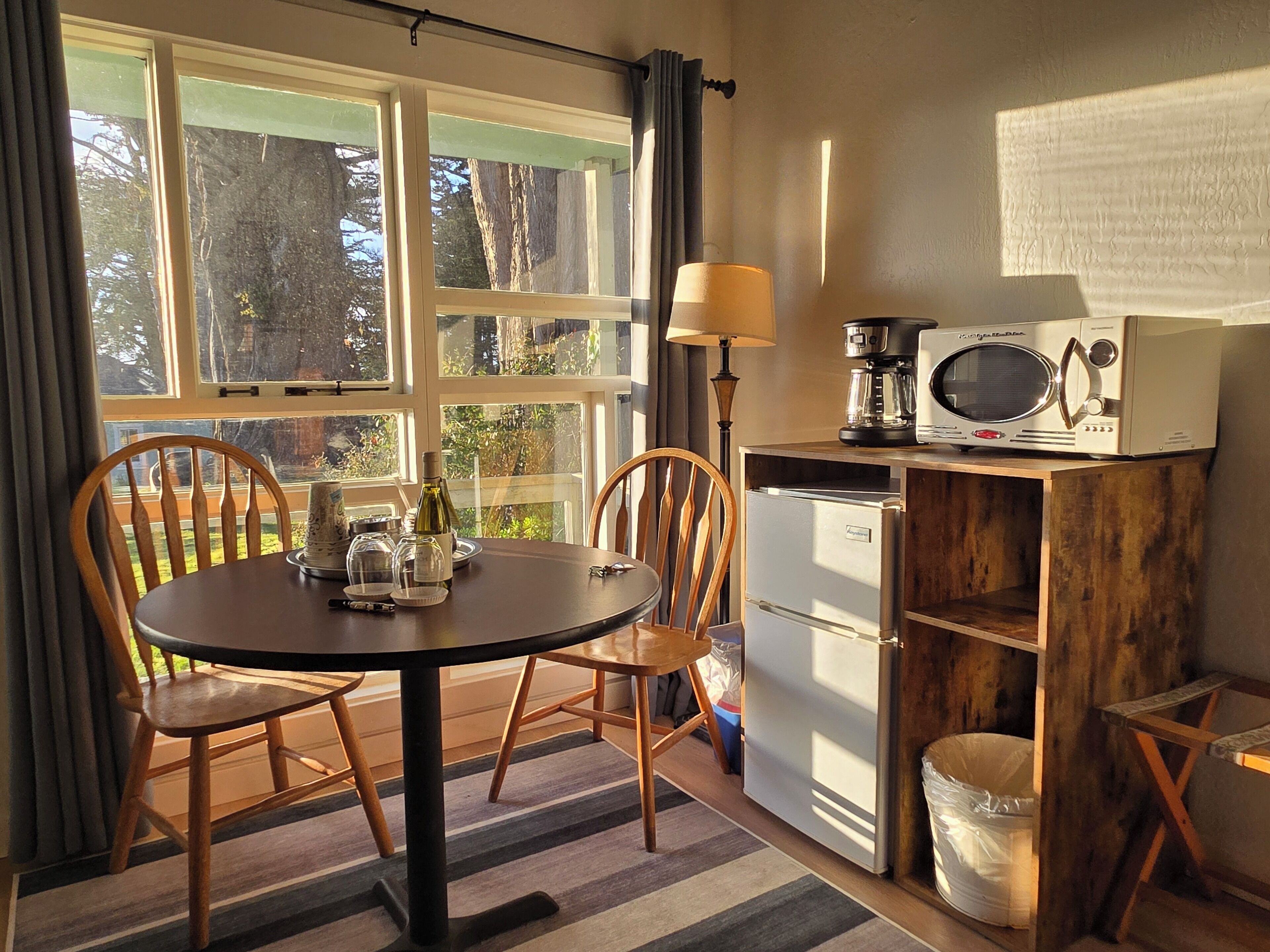 A compact kitchen with a dining table, chairs, a refrigerator, a microwave, and a coffee maker.