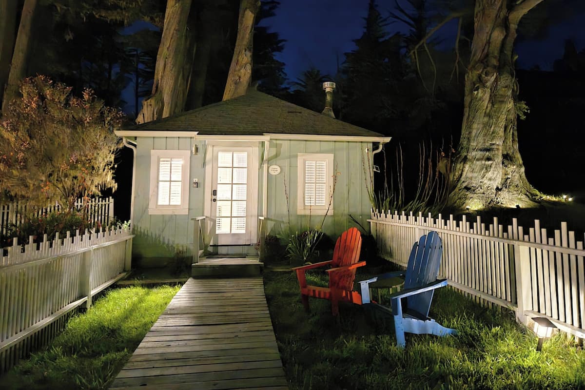 A small, single-story house with a front porch, a wooden deck, and a white picket fence.
