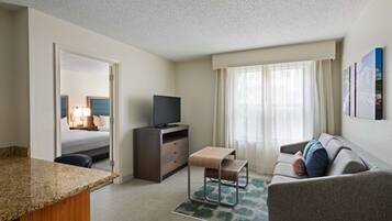 A hotel room with a bed, a TV, a desk, a sofa, and a window with curtains.