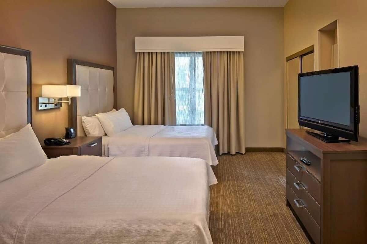 Habitación de hotel con dos camas, un televisor en una cómoda, una mesita de noche y una ventana con cortinas.