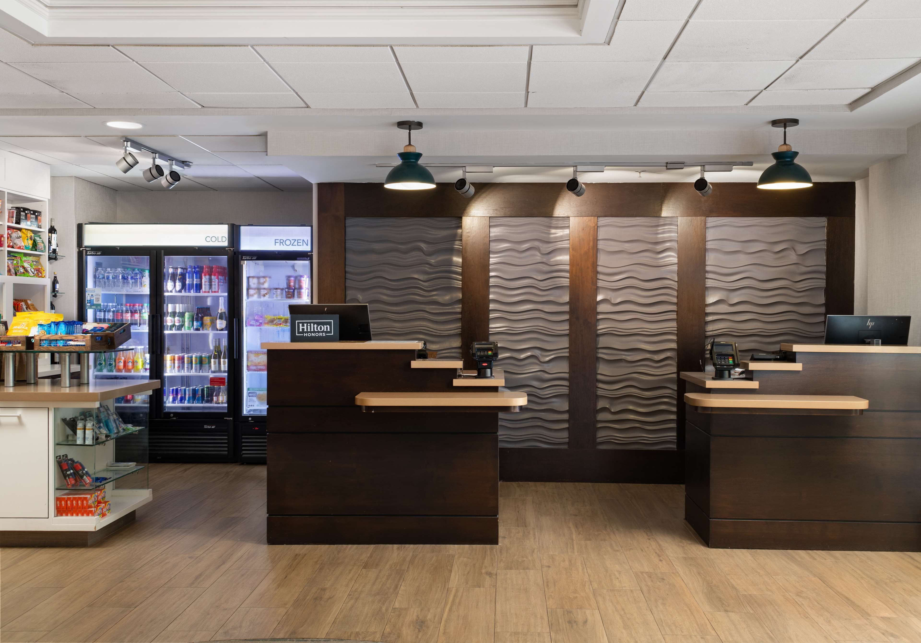 Zona de recepción de un hotel con un mostrador de madera, un minibar y un refrigerador lleno de bebidas.