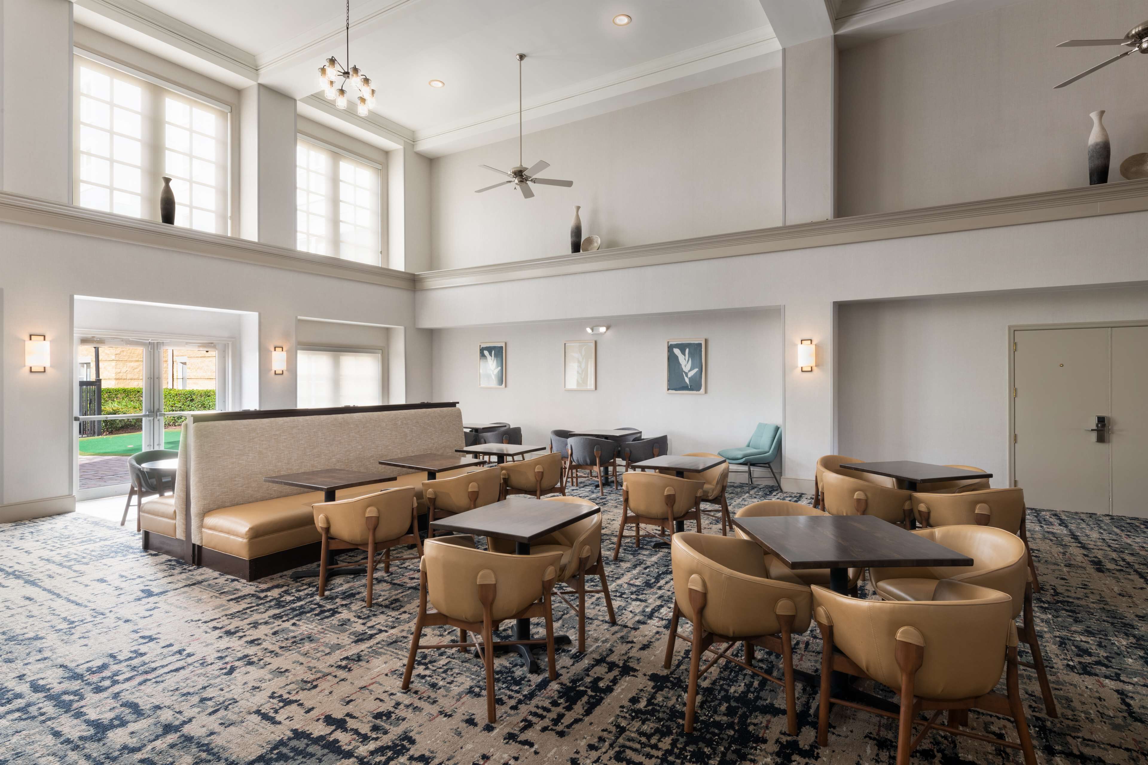 A spacious hotel lobby with high ceilings, large windows, and a mix of seating areas including tables and chairs.