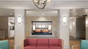 Eine Lobby mit einem roten Sofa, blaugrünen Sesseln, einem Kamin und einem Schild für die Toiletten.