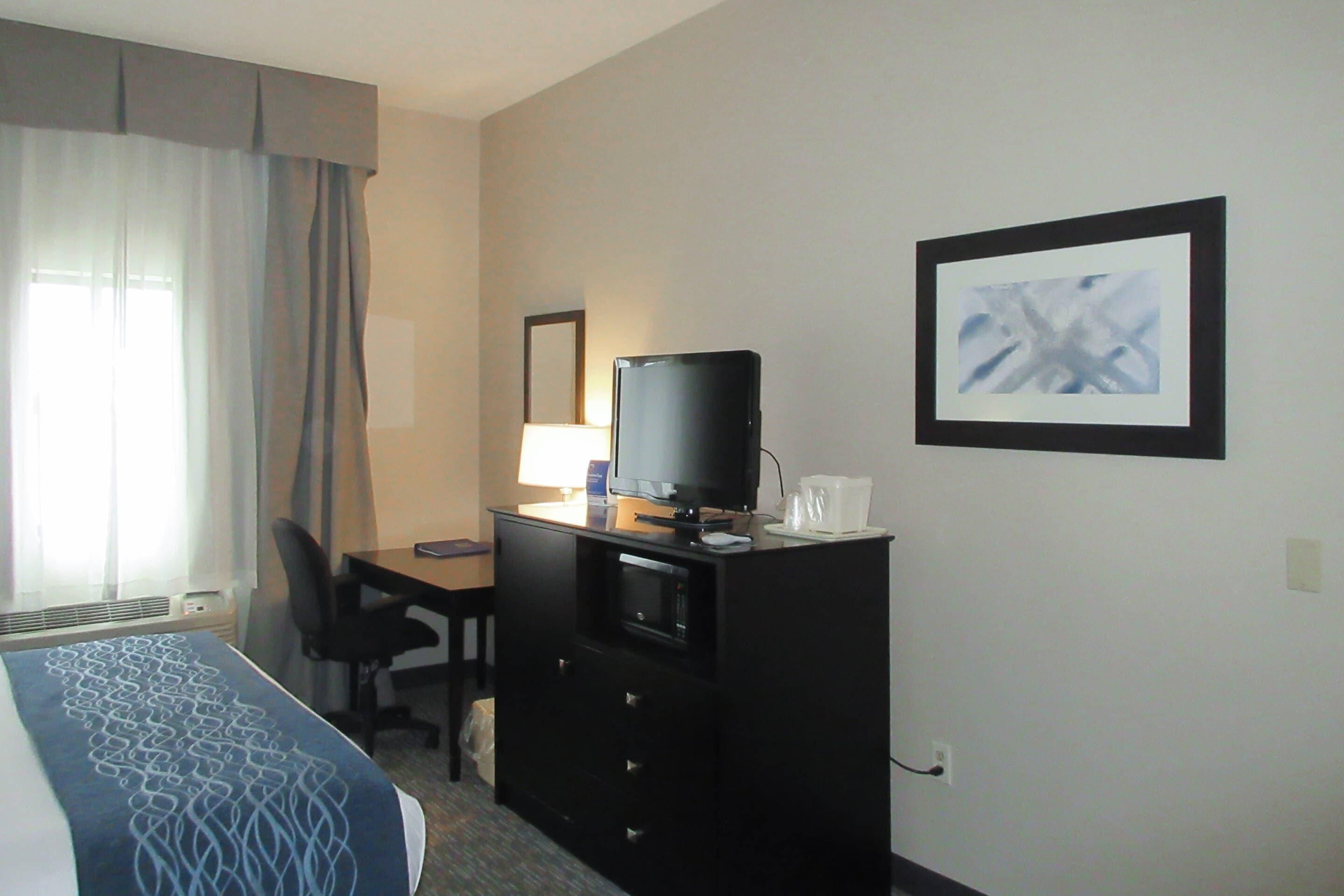 A hotel room with a bed, a desk with a computer, a television, and a framed picture on the wall.