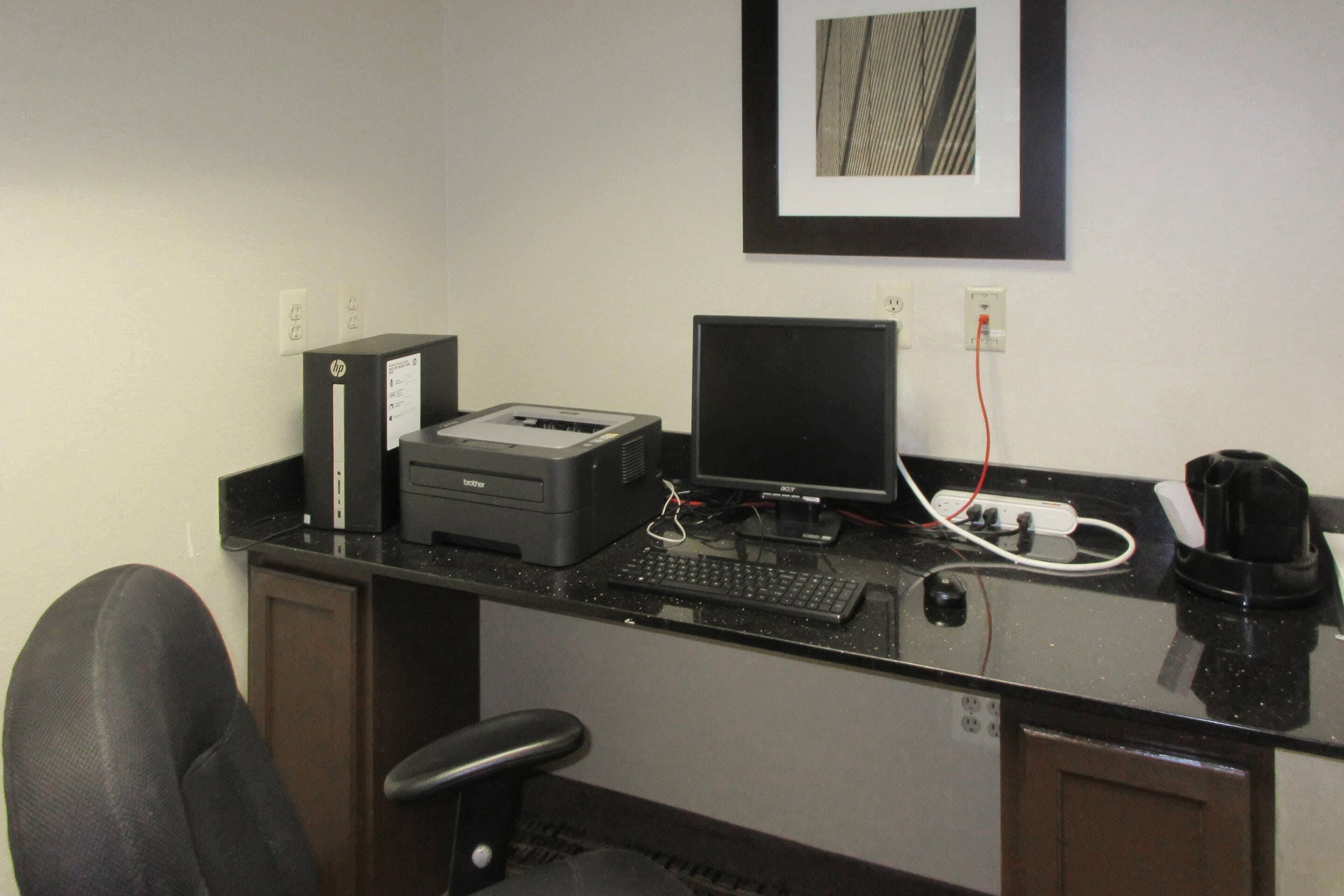 A small office with a desk, chair, printer, monitor, and coffee machine.
