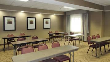 Un salón de conferencias con mesas y sillas, cuadros en la pared y un amplio ventanal con cortinas.